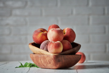 Peaches in wooden bowl with white brick wall background