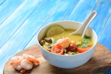 Tom Yam kung Spicy Thai soup with shrimp, seafood,tomatoes, mushrooms, lemongrass, coconut milk, ginger and chili pepper in bowl . Traditional Thai food