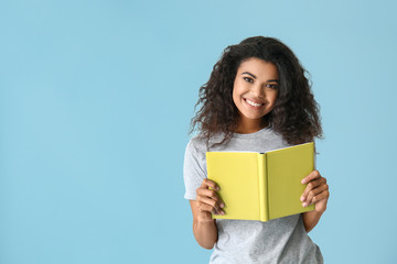 Portrait of happy African-American woman with book on color background