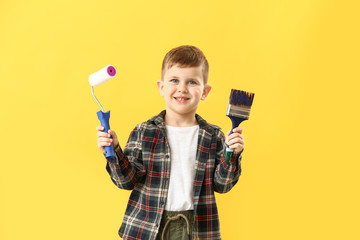 Cute little boy with paint roller and brush on color background