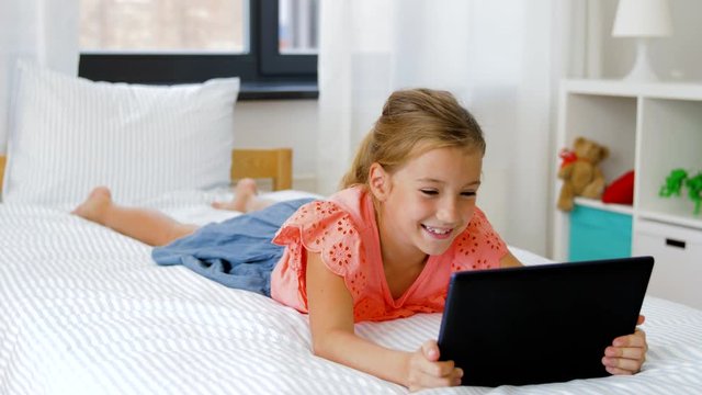children, technology and communication concept - smiling girl having vide call on tablet computer lying on bed at home