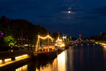 Fototapeta na wymiar Night view of illuminated restaurant ships with reflection in the water of the river Auraioki, the night landscape of Turku with illumination, the life of the night city. City of Turku, Finland.