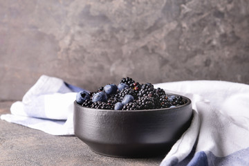 Fototapeta na wymiar Bowl with tasty blackberries and blueberries on grey table