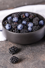 Bowl with tasty blackberries and blueberries on grey table