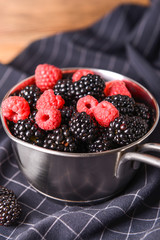 Pot with tasty blackberries and raspberries on table
