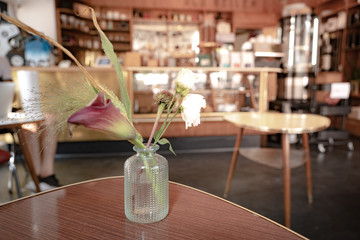 Interior selected focus and close up view at flower in the vase on wooden table and blur background of vintage cozy cafe or coffee shop.