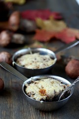 Julienne with forest mushrooms. Mushrooms are baked in cream and with cheese. Autumn leaves.