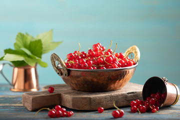 Red currant in a metal bowl on wooden background