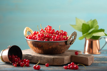 Red currant in a metal bowl on wooden background