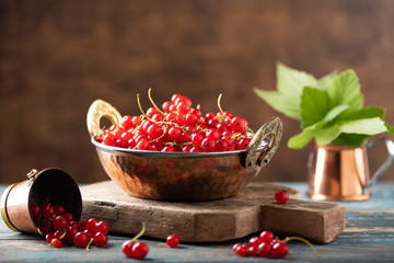 Red currant in a metal bowl on wooden background