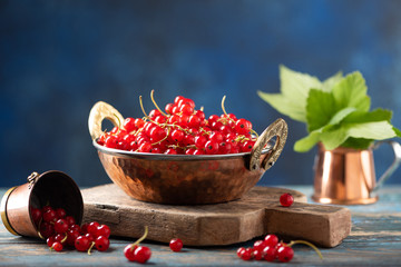 Red currant in a metal bowl on wooden background
