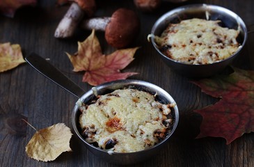 Julienne with forest mushrooms. Mushrooms are baked in cream and with cheese. Autumn leaves.
