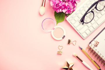 Female workspace with laptop, pink hydrangea, golden accessories, pink diary on pink background.