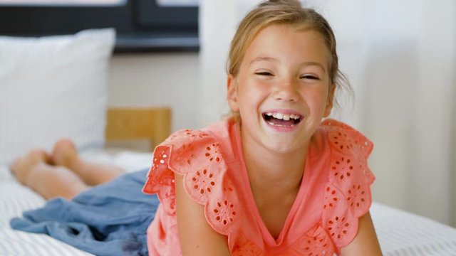 childhood, emotion and people concept - happy smiling beautiful girl lying on bed at home