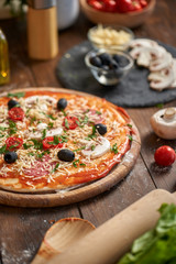 Homemade Pizza on wooden board, with tomatoes and salami, mushrooms, Italian style on old wooden table.