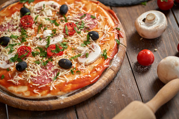 Homemade Pizza on wooden board, with tomatoes and salami, mushrooms, Italian style on old wooden table.