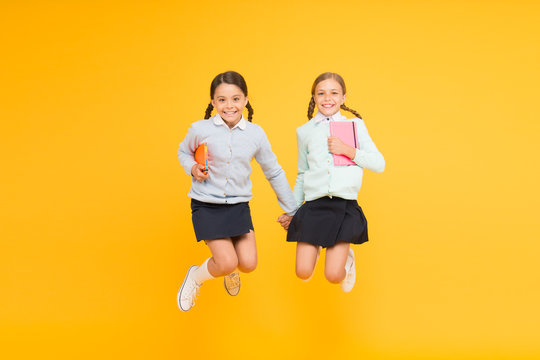 Happy to be back to school. Elementary school pupils in mid air. Little girls jumping with books on yellow background. Small kids enjoying school break time. Welcome the children to school