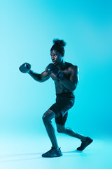 Fototapeta na wymiar confident african american sportsman in shorts and sneakers boxing on blue background