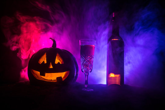 Two glasses of wine and bottle with Halloween - old jack-o-lantern on dark toned foggy background. Scary Halloween pumpkin
