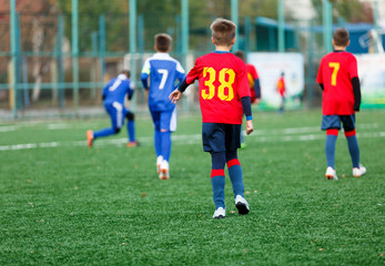 Obraz premium Boys in white and blue sportswear plays football on field, dribbles ball. Young soccer players with ball on green grass. Training, football, active lifestyle for kids concept 