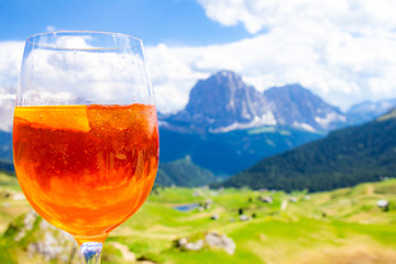 View of the traditional Italian alcoholic drink Aperol Spritz on the background of colorful Italian meadows and the Dolomites Alps mountains. village St. Cristina di Val Gardena Bolzano Seceda, Italy.