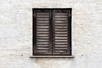 Obraz premium Closed dilapidated wooden window blinds with faded color and rusted metal hinges mounted on dirty family house wall at old part of town on warm sunny spring day