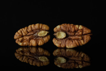Group of two whole fresh brown pecan nut half isolated on black glass