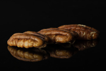 Group of three whole fresh brown pecan nut half in a row isolated on black glass