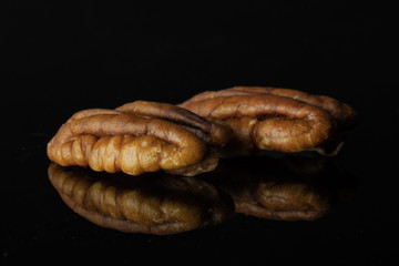 Group of two whole fresh brown pecan nut half in a row isolated on black glass