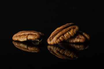 Group of three whole unshelled fresh brown pecan nut half isolated on black glass