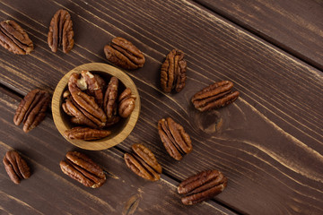 Lot of whole fresh brown pecan nut half in a wooden bowl flatlay on brown wood