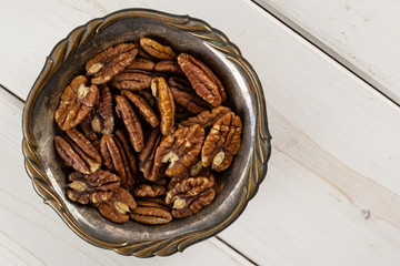 Lot of whole fresh brown pecan nut half in old iron bowl flatlay on white wood