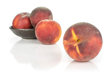 Group of four whole fresh red peach one is in the front and the rest is in the back in a dark ceramic bowl isolated on white background