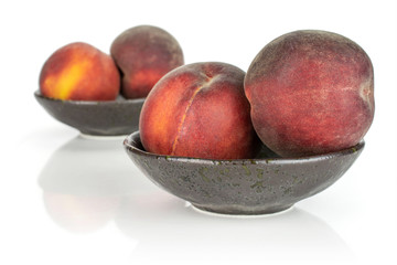 Group of four whole fresh red peach in a dark ceramic bowl isolated on white background