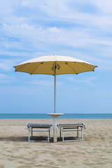 Pair of sun loungers and a beach umbrella on a deserted beach. Vacation and leisure concept