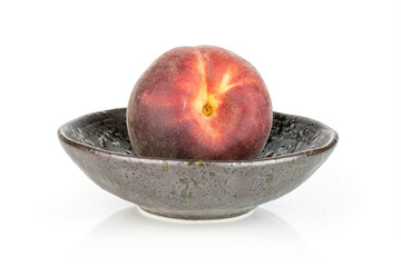 One whole fresh red peach in a dark ceramic bowl isolated on white background