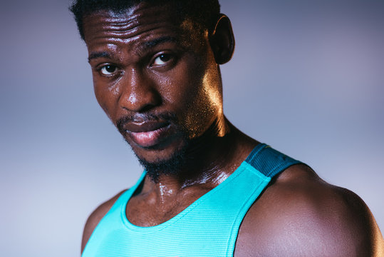 handsome, confident african american sportsman with sweaty face looking at camera on grey and blue gradient background with lighting
