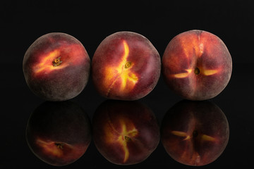 Group of three whole fresh red peach in a row isolated on black glass