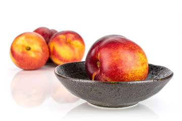 Group of four whole fresh red nectarine in a dark ceramic bowl isolated on white background