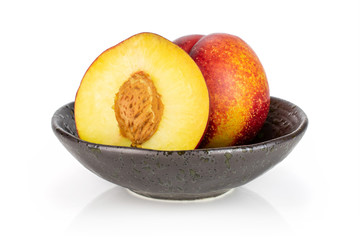 Group of one whole one half of fresh red nectarine in a dark ceramic bowl isolated on white background