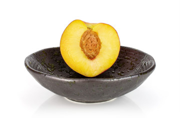 One half of fresh red nectarine in a dark ceramic bowl isolated on white background