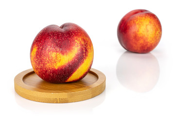 Group of two whole fresh red nectarine on a round bamboo coaster isolated on white background