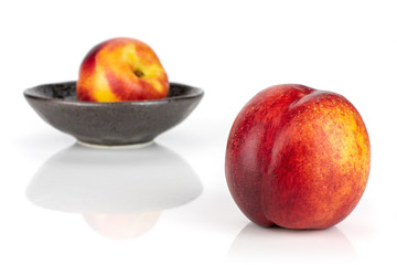 Group of two whole fresh red nectarine one is in the front and the other is in the back in a dark ceramic bowl isolated on white background