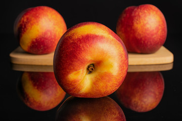 Group of three whole fresh red nectarine on a bamboo cutting board isolated on black glass
