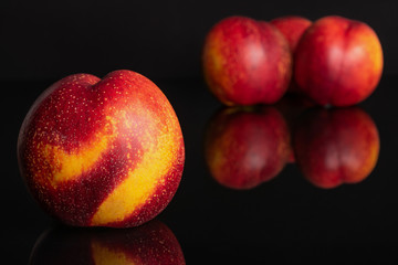 Group of four whole fresh red nectarine one is in the front and the rest is in the back isolated on black glass