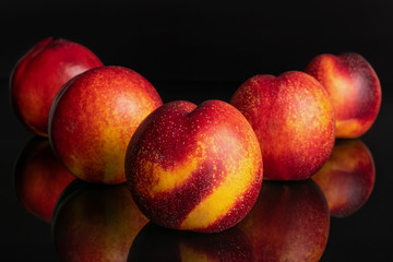 Group of five whole fresh red nectarine one is in the front and the rest is layered diagonally isolated on black glass