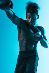 shirtless, muscular african american sportsman boxing on blue background