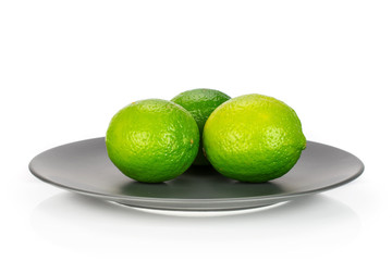 Group of three whole fresh green lime on a ceramic grey plate isolated on white background
