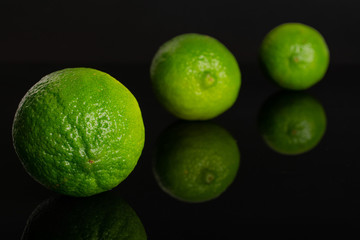 Group of three whole fresh green lime placed diagonally in a line isolated on black glass
