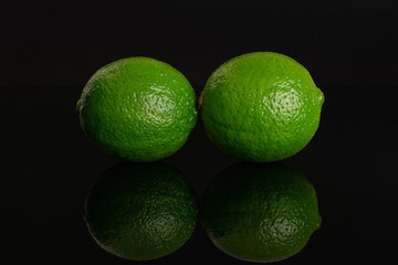 Group of two whole fresh green lime isolated on black glass